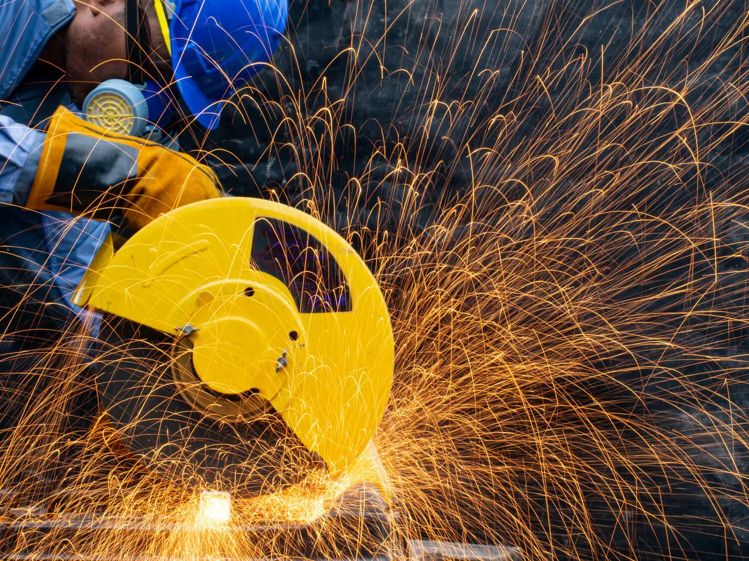 A person wearing protective gear while cutting metal with a miter saw