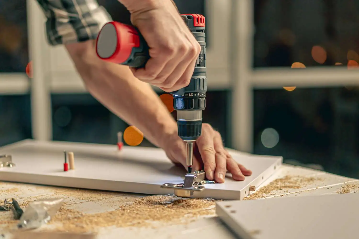 Installing hinges on a cabinet door with a cordless drill.